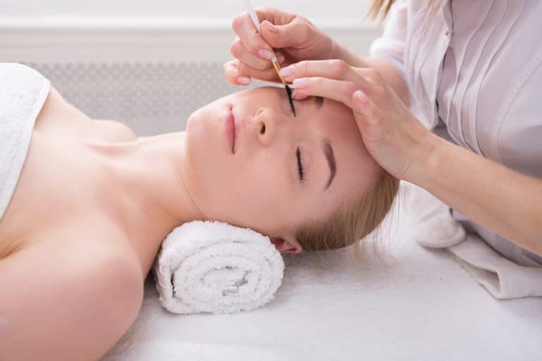 Woman gets eyelashes tinting by beautician at spa